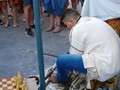 A man at a Moorish street festival carving chess pieces using his feet.